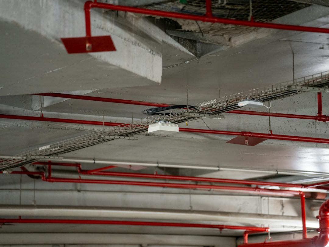 Exposed concrete ceiling with red sprinkler pipes and cable trays