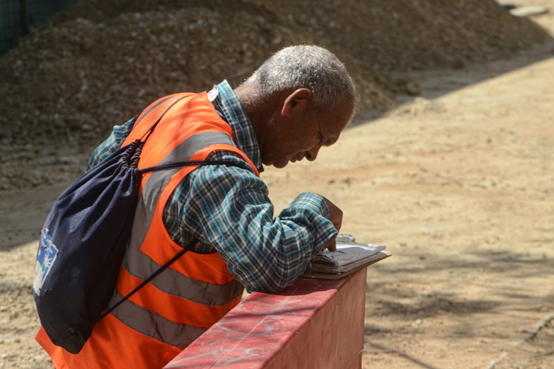 A worker in an orange vest writing notes on a clipboard on site